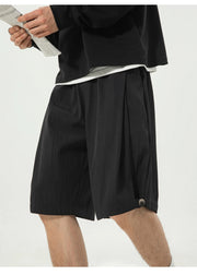 A person wearing black pleated shorts with a white undershirt peeking out at the hem, photographed against a plain light background.