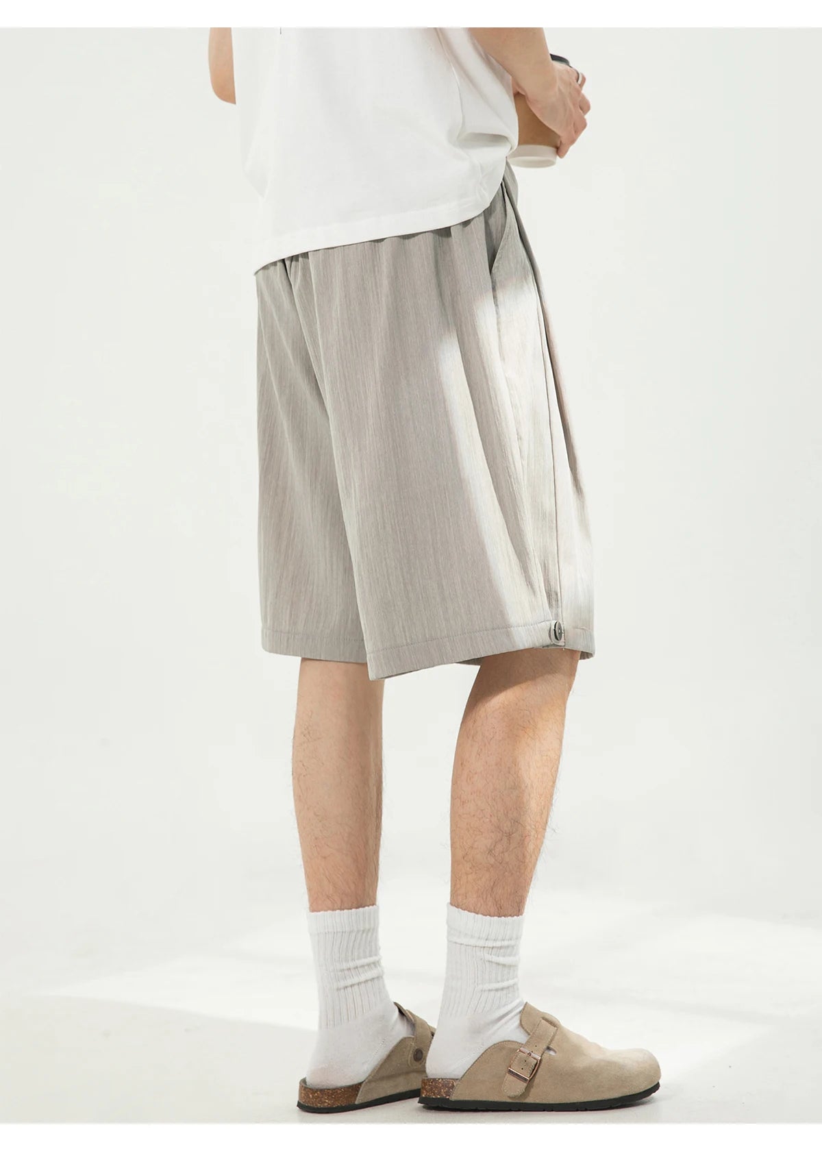 A person shown from the waist down wearing light beige wide-leg shorts, white crew socks, and tan slip-on loafers against a plain white studio background.