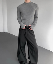 Person wearing a gray long-sleeve shirt and black wide-leg pants against a plain background
