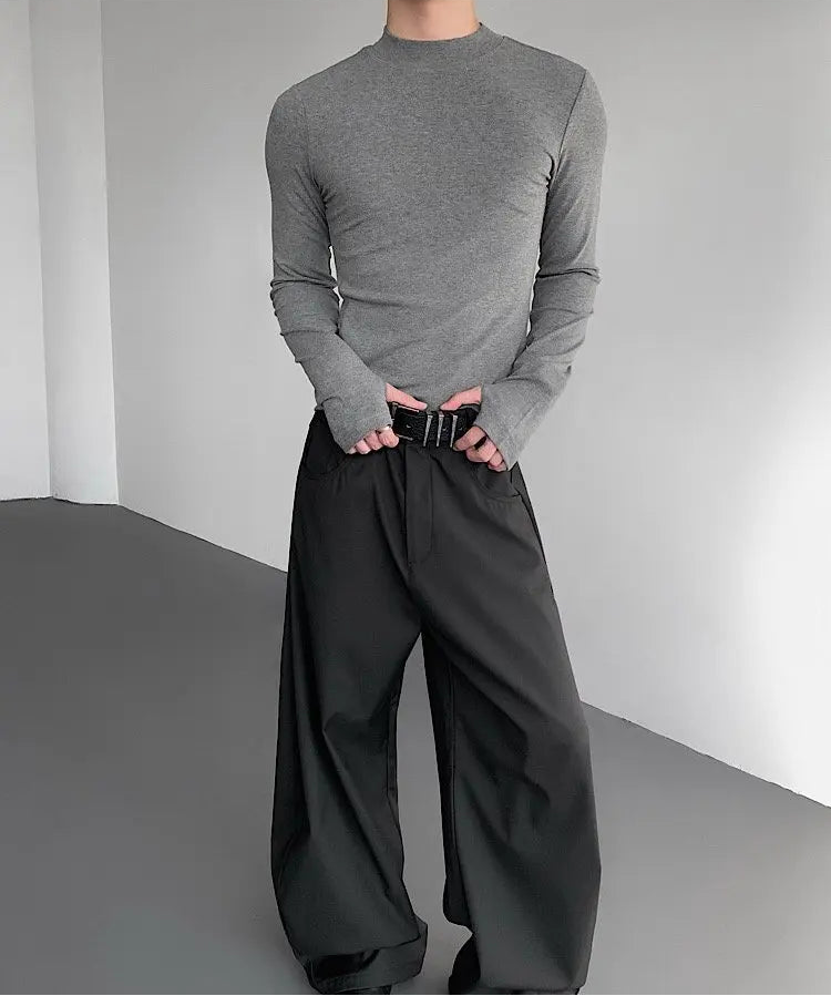 Person wearing a gray long-sleeve shirt and black wide-leg pants against a plain background