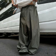 A person wearing extremely baggy, wide-leg olive green pants and a white t-shirt, standing outdoors next to a white vehicle.