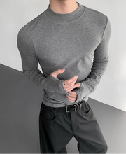 Person wearing a gray long-sleeve shirt and dark pants on a plain background