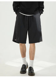 A person wearing black wide-leg shorts with a white waistband, styled with a black sweatshirt, white socks, and black loafers against a plain light background.