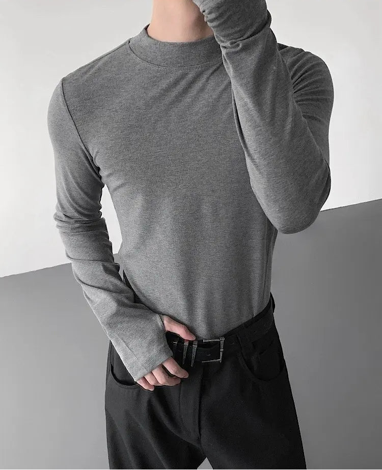 Person wearing a gray long-sleeve shirt and dark pants against a neutral background