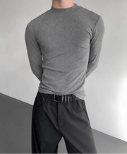 Person wearing a gray long-sleeve shirt and black pants against a neutral background