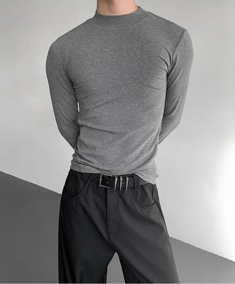 Person wearing a gray long-sleeve shirt and black pants against a neutral background