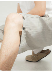 Close-up of a person wearing light beige textured shorts with a button closure and drawstring detail, paired with a white top and tan slip-on shoes.