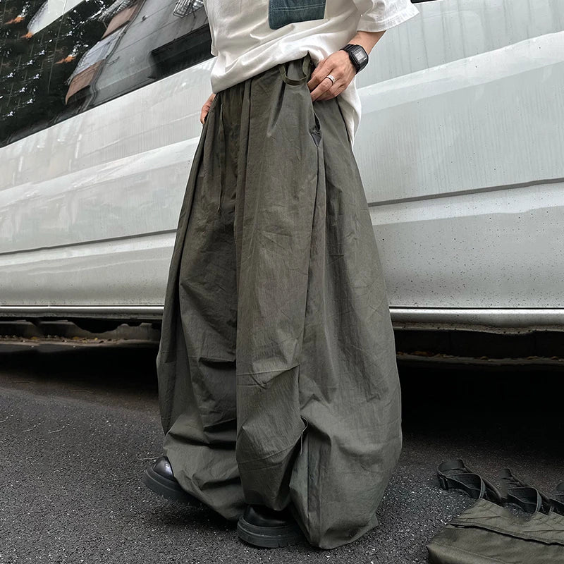 A person wearing extremely loose, wide-leg olive green cargo pants, paired with a white t-shirt and black shoes, standing outdoors next to a white vehicle.