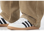 White sneakers with black stripes worn with beige corduroy pants on a white background