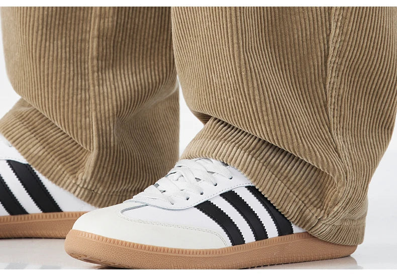 White sneakers with black stripes worn with beige corduroy pants on a white background