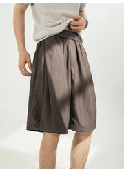 A person wearing loose, high-waisted brown shorts with a gathered elastic waistband and a light beige knit top, shown against a plain light background.