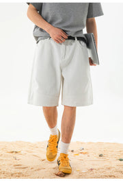 A person wearing light off-white or cream-colored knee-length shorts, a gray t-shirt, white socks, and yellow sneakers, standing on a sandy surface against a white background.