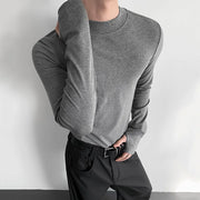 Person wearing a gray long-sleeve shirt and black pants against a white background