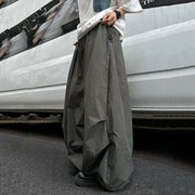 A person wearing very wide-leg, loose-fit dark gray cargo pants and a white shirt, standing on asphalt next to a white vehicle.