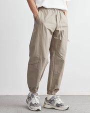 Person wearing beige jogger pants and gray sneakers on a plain background