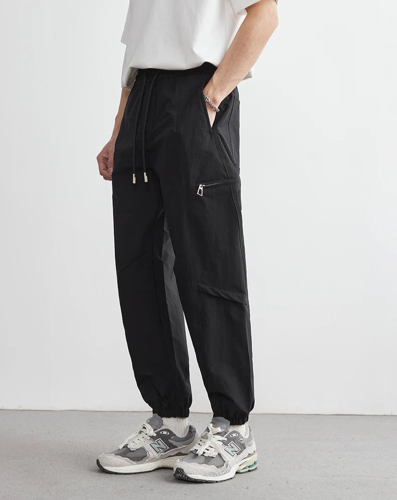 Person wearing black cargo pants and white sneakers on a plain background