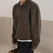 Person wearing a brown sweater holding a brown bag against a neutral background