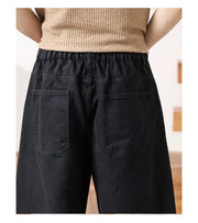 Rear view of a person wearing loose black wide-leg pants with a drawstring waistband and large patch pockets, paired with a beige knit top.