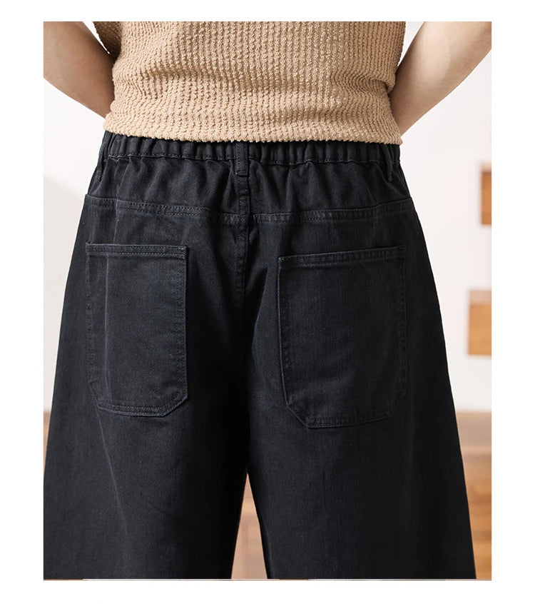 Rear view of a person wearing loose black wide-leg pants with a drawstring waistband and large patch pockets, paired with a beige knit top.