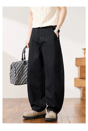 A model wearing black wide-leg baggy pants, a cream ribbed tank top, and beige shoes, holding a black and white patterned handbag in a minimalist indoor setting.