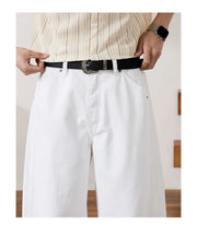 A cropped apparel detail shot showing a person from the chest down wearing a cream striped button-up shirt tucked into white trousers with a black belt and silver buckle. 