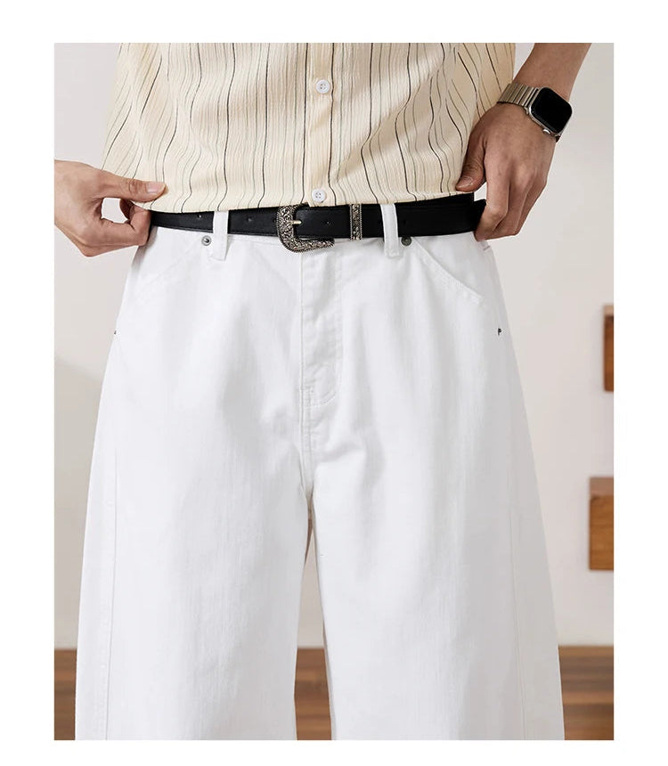 A cropped apparel detail shot showing a person from the chest down wearing a cream striped button-up shirt tucked into white trousers with a black belt and silver buckle. 