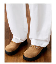 A person wearing white wide-leg pants and tan suede lace-up shoes with black soles, standing on a wooden floor. Chinese text appears below the photo.