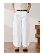 A model wearing white wide-leg pants with a black belt, paired with a cream ribbed top and tan shoes, shown in a styled indoor setting with wooden stairs.