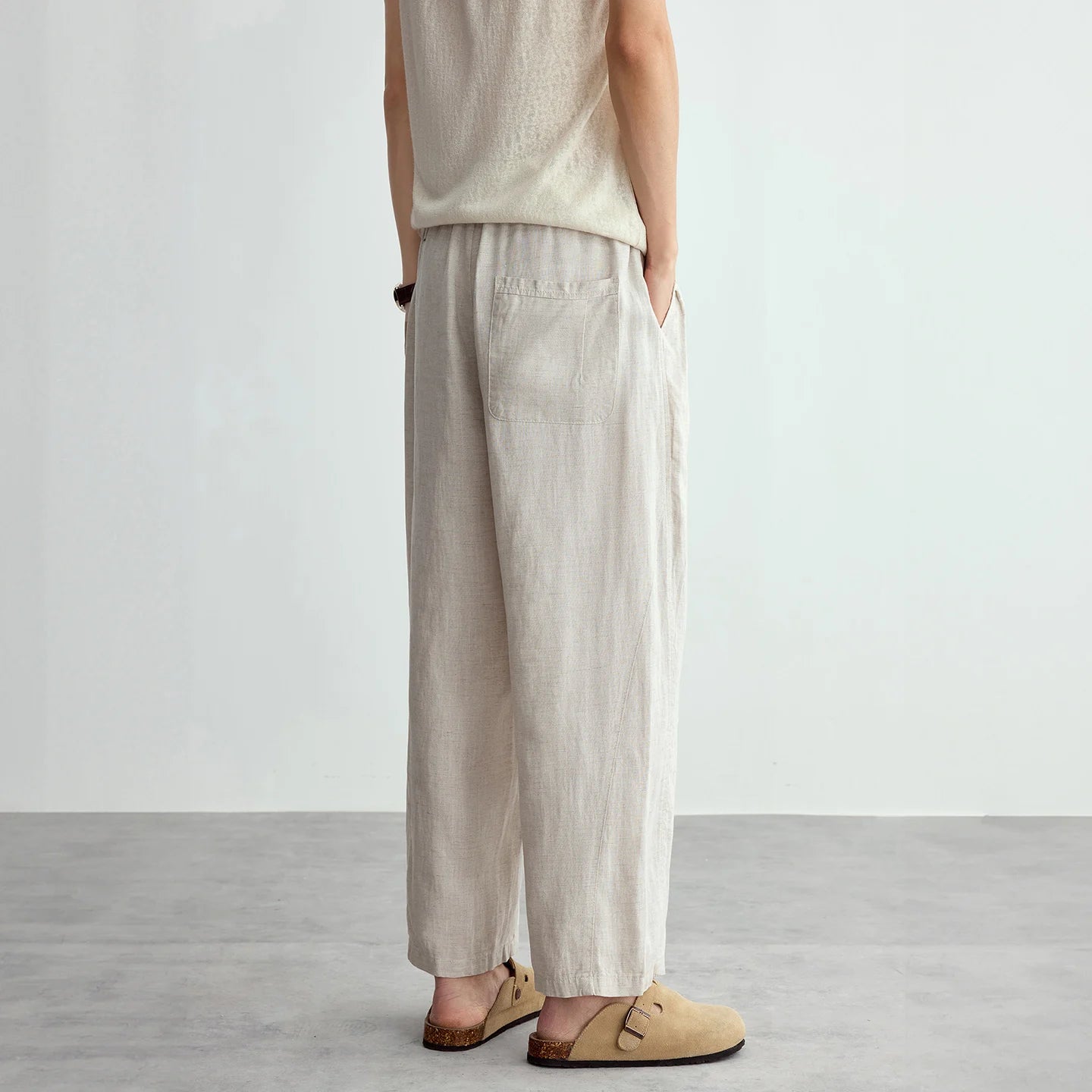 Person wearing beige sleeveless top and wide-leg pants on a plain background