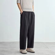 Person wearing black wide-leg pants and a beige knit sweater on a light gray background