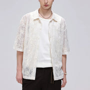A model wearing a white lace short-sleeve button-up shirt over a white ribbed t-shirt and black pants, photographed against a light gray studio background.