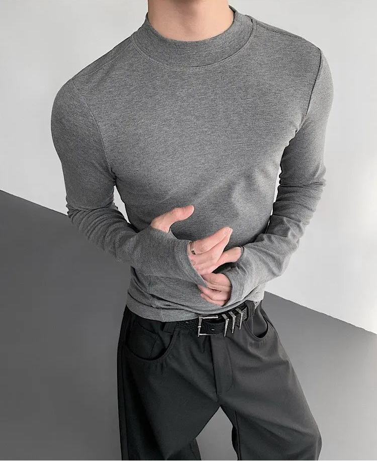 Person wearing a gray long-sleeve shirt and dark pants on a plain background