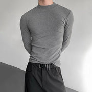 Person wearing a gray long-sleeve shirt and black pants against a neutral background