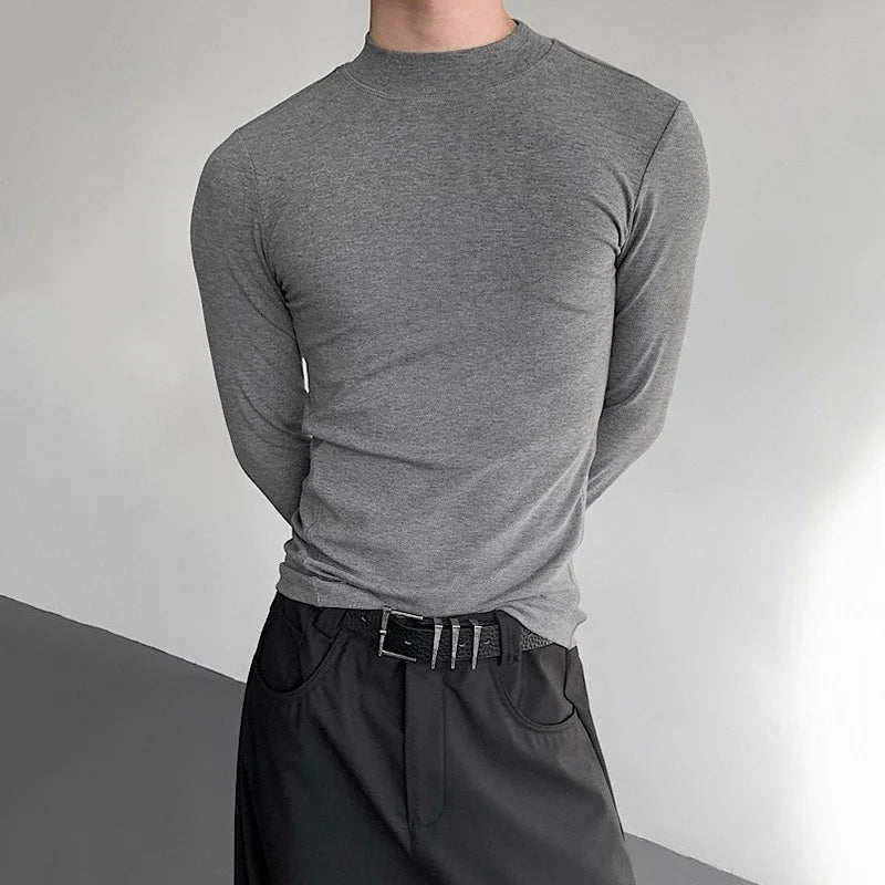 Person wearing a gray long-sleeve shirt and black pants against a neutral background