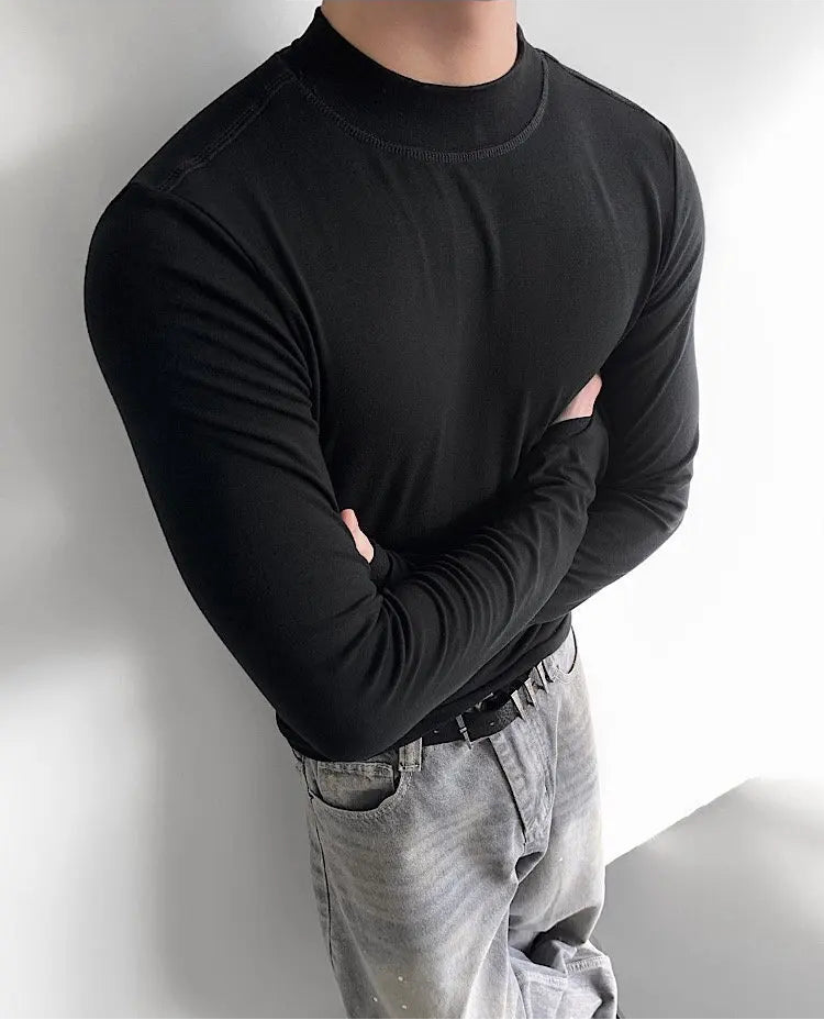 Person wearing a black turtleneck and light gray pants against a white wall
