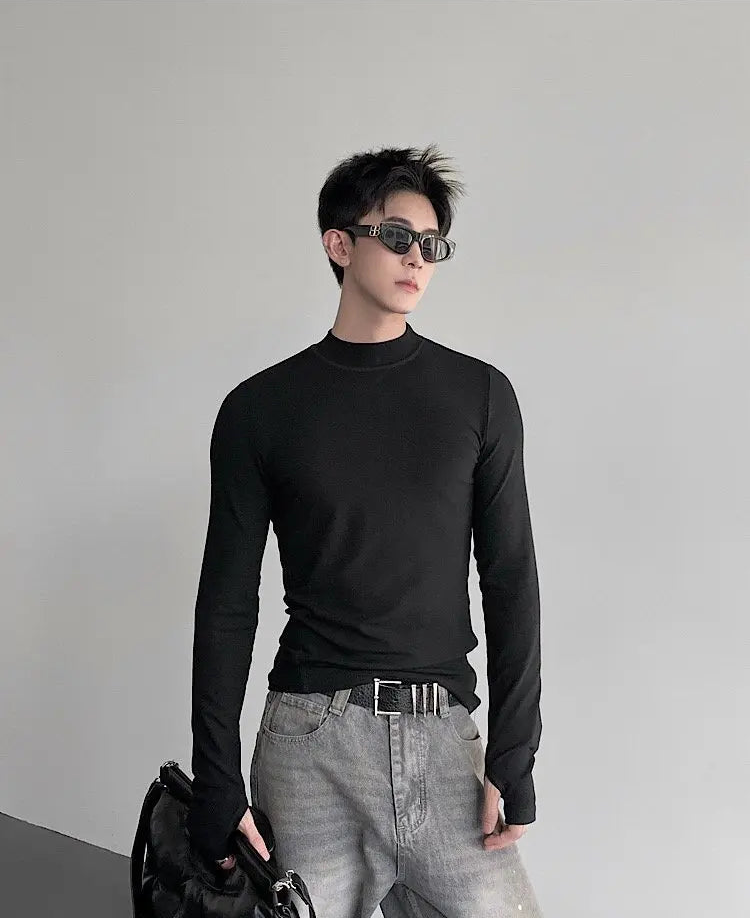 Man wearing a black long-sleeve shirt and gray pants against a plain background