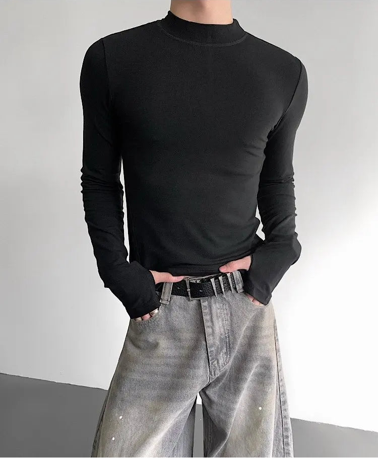 Person wearing a black long-sleeve top and gray pants against a plain background