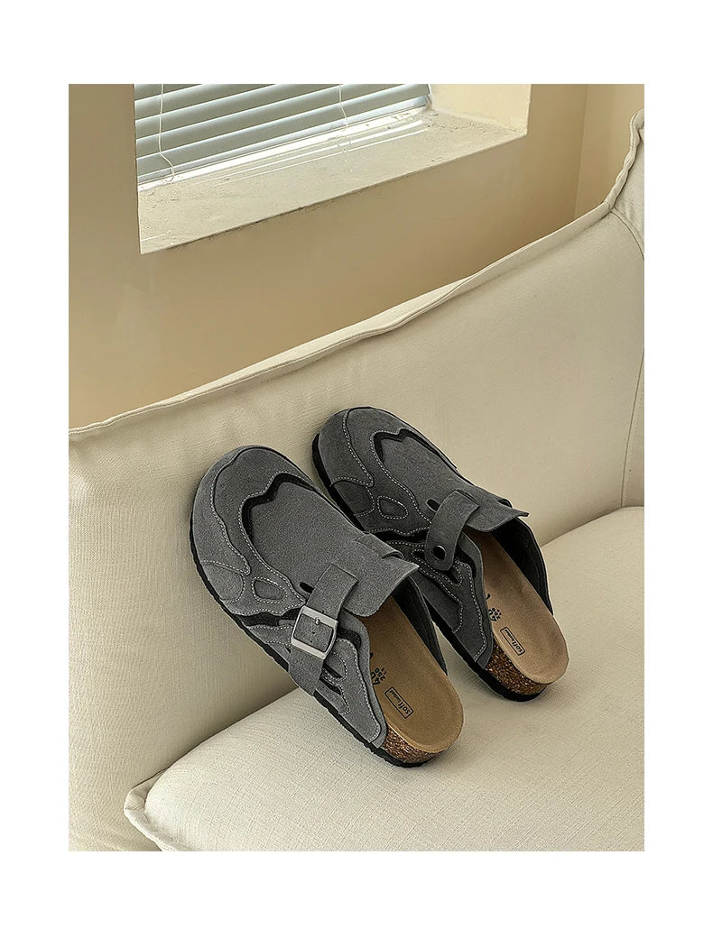 Pair of gray sandals on a beige cushioned surface with a window in the background.