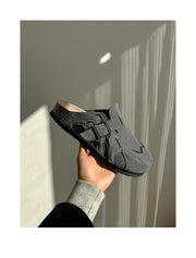 Hand holding a black sandal against a neutral background