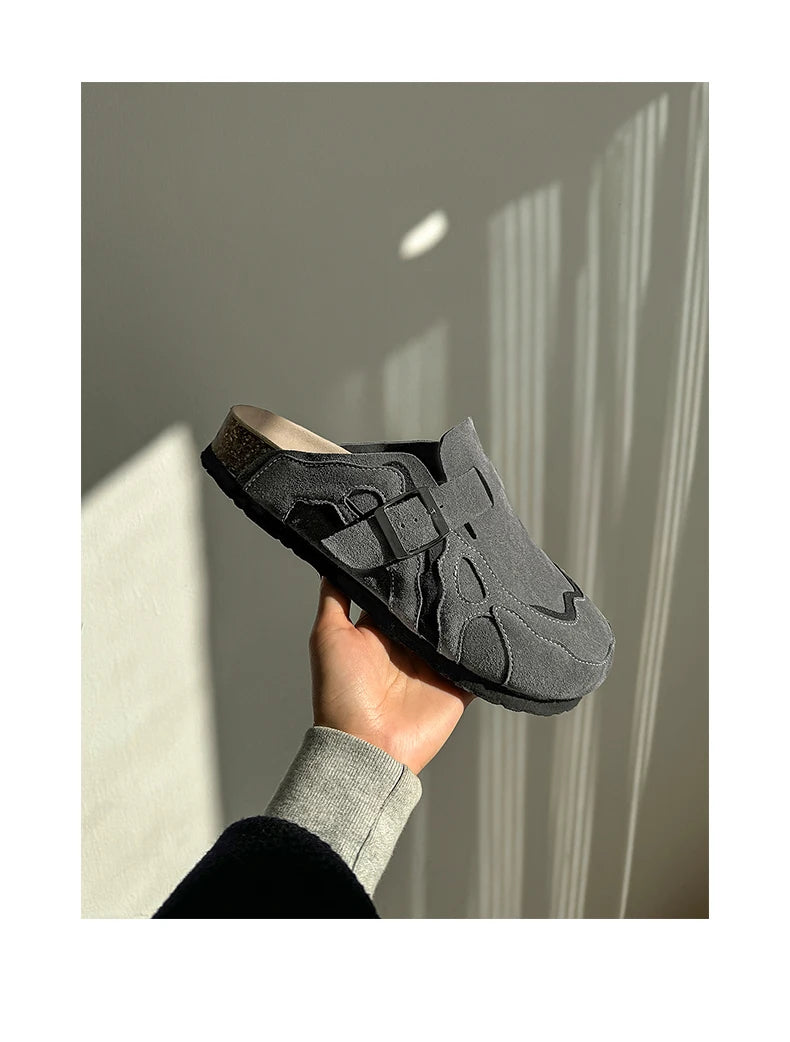 Hand holding a black sandal against a neutral background