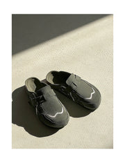 Pair of black shoes on a textured beige surface with a soft shadow.