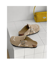 Pair of beige sandals with a strap on a tiled floor next to a yellow bag.