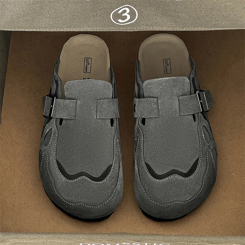 A pair of gray slip-on clogs with strap closures, photographed from above inside a brown shoebox.