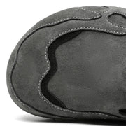 Close-up of a dark gray suede shoe upper with decorative stitching and a wavy black accent panel, photographed on a white background.