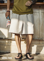 Person wearing a green shirt and beige shorts, standing against a wooden wall.