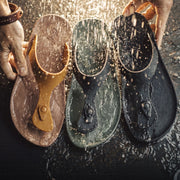 Three pairs of sandals in different colors held by hands against a dark background.