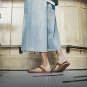 Person wearing light blue denim pants and brown sandals on a neutral background