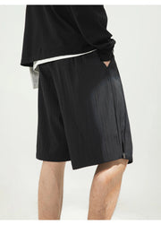 A close-up of a person wearing black textured shorts with a side pocket and a black top, photographed against a plain light background.